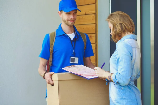 Repartidor sonriente con uniforme azul que entrega la caja de paquetes al destinatario: concepto de servicio de mensajería. Repartidor sonriente en uniforme azul — Foto de Stock