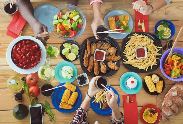Ahşap masada otururken birlikte yemek yiyen bir grup insanın üst düzey görüntüsü. Masada yemek var. İnsanlar fast food yiyor..
