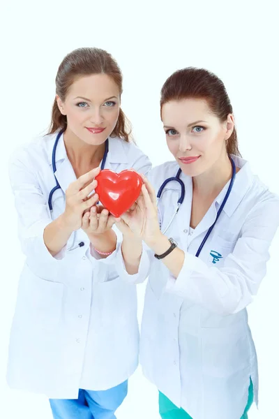 Duas médicas segurando um coração vermelho, isoladas em fundo branco. Duas mulheres doutor — Fotografia de Stock