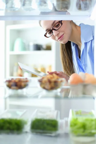 Retrato de una mujer parada cerca de una nevera abierta llena de alimentos saludables, verduras y frutas. — Foto de Stock