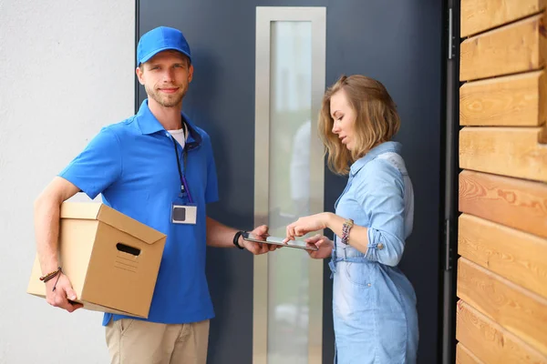 Leende leverans man i blå uniform leverera paket låda till mottagaren - kurir service koncept. Leende leverans man i blå uniform — Stockfoto