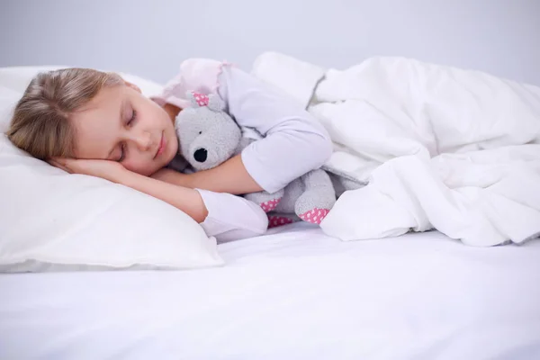 Criança menina dorme na cama com um brinquedo ursinho de pelúcia . — Fotografia de Stock