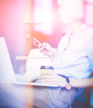 Ofis masasında dizüstü bilgisayarıyla oturan genç bir kadın. Pencereden bakıyor. Genç kadın.