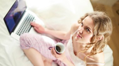 Dizüstü bilgisayar ile yatakta oturan genç güzel kadın.
