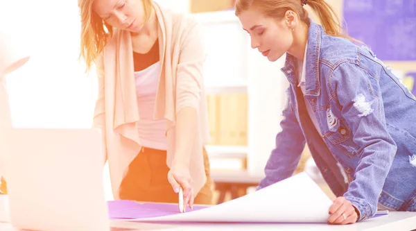 Twee jonge vrouw in de buurt van bureau met instrumenten, plan en laptop. — Stockfoto