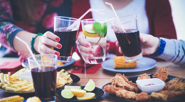 Ahşap masada otururken birlikte yemek yiyen bir grup insanın üst düzey görüntüsü. Masada yemek var. İnsanlar fast food yiyor..