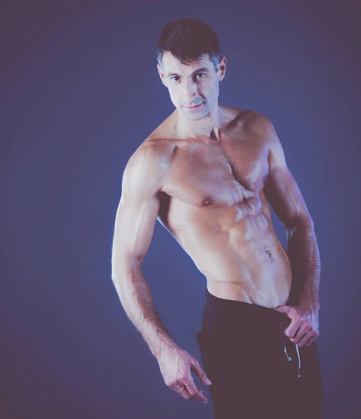 Uomo muscoloso. Uomo muscoloso su uno sfondo grigio che mostra muscoli. Istruttore di fitness. Professionista di fitness. Allenati. Mens fitness . — Foto Stock