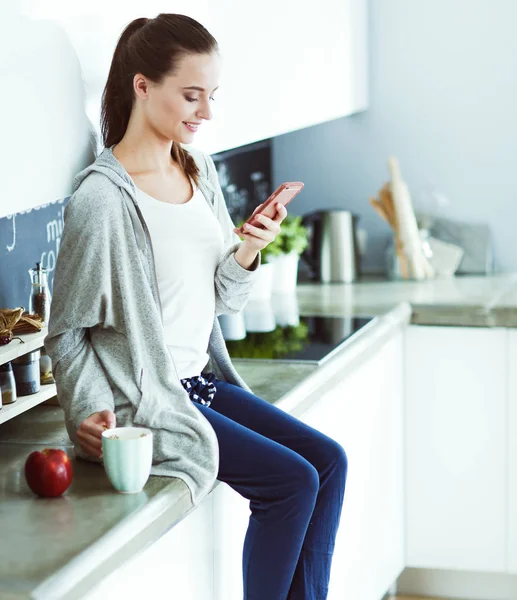 modern mutfakta otururken cep telefonu kullanan kadın.