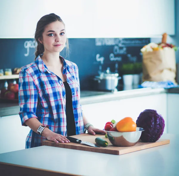 Masanın yanındaki mutfakta sebze doğrayan genç bir kadın..