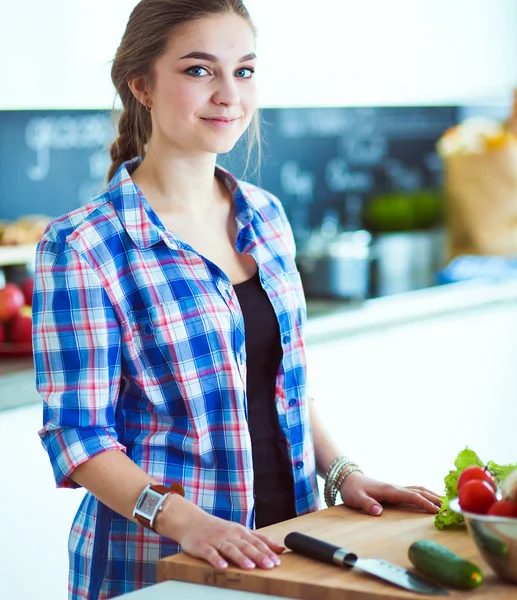 Masanın yanındaki mutfakta sebze doğrayan genç bir kadın..