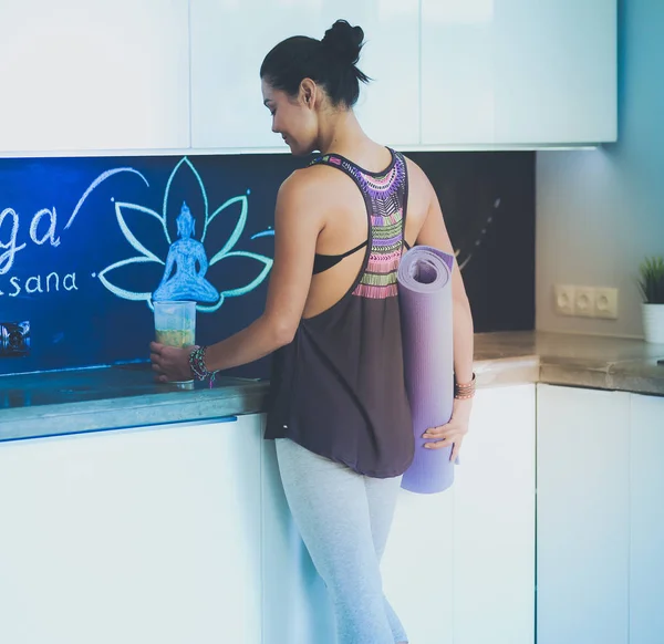 Retrato de una mujer sonriente sosteniendo en su mano una esterilla de yoga mientras estaba de pie en el estudio. Yoga. Una mujer. Bienestar — Foto de Stock