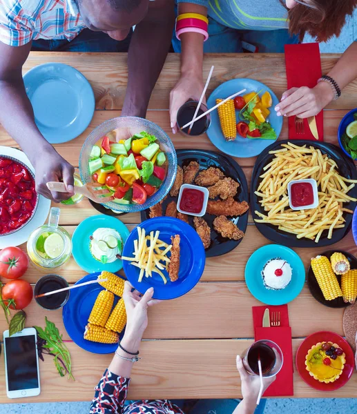 Ahşap masada otururken birlikte yemek yiyen bir grup insanın üst düzey görüntüsü. Masada yemek var. İnsanlar fast food yiyor..