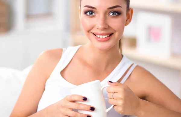 Junge schöne Frau mit einer Tasse auf dem Sofa zu Hause — Stockfoto