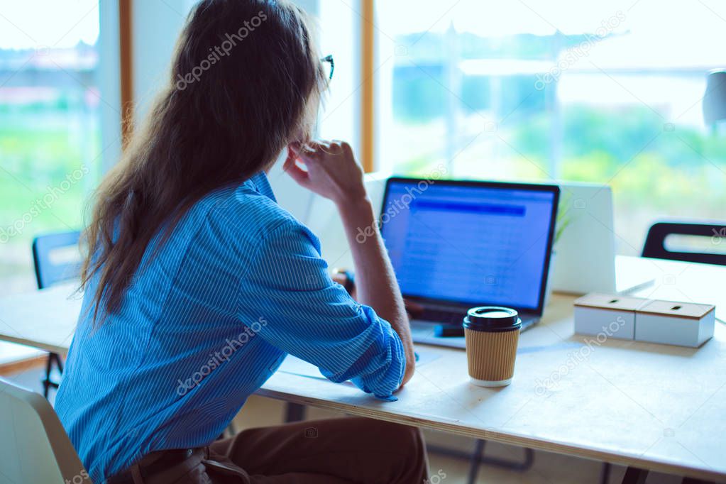 Young woman sitting in office table, looking at laptop computer screen . Young woman