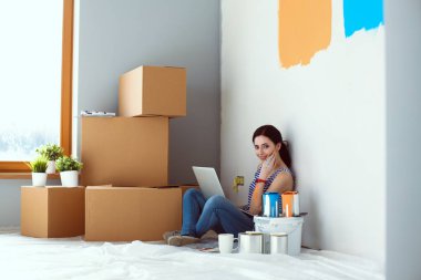 Yeni daire dizüstü bilgisayar ile oturup, boyama sırasında genç kadın portre. Dizüstü bilgisayar ile genç kadın