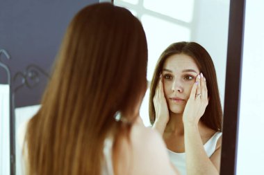 Genç kadın kendini evde aynada yansıma arıyor.