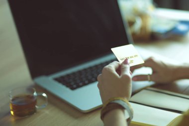 Kredi kartı tutan ve dizüstü bilgisayar kullanan genç bir kadın. Çevrimiçi alışveriş kavramı