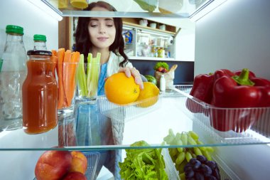 Sağlıklı yiyecek, sebze ve meyvelerle dolu açık buzdolabının yanında duran kadın portresi. Kadın portresi