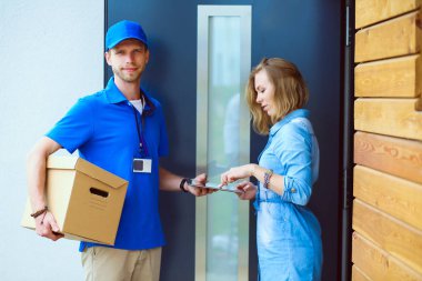 Mavi üniformalı gülümseyen kurye servis konseptine paket kutusu teslim eden teslimatçı. Mavi üniformalı gülümseyen teslimatçı.