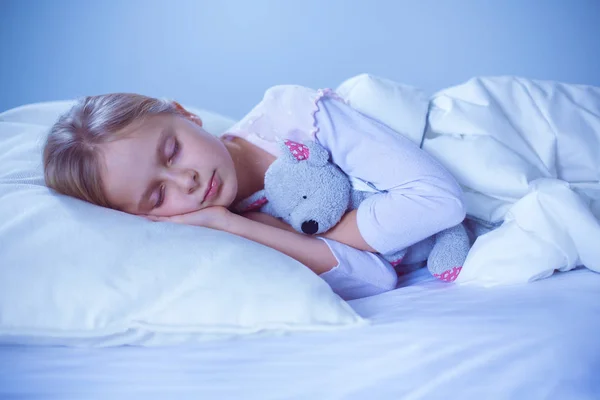 Kind meisje slaapt in het bed met een speeltje teddy beer. — Stockfoto