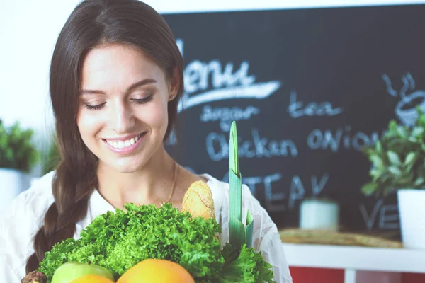 Smiling young woman holding vegetables standing in kitchen. Smiling young woman — Stock Photo, Image