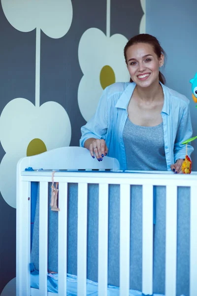 Mujer joven parada cerca de la cuna de los niños. Mamá joven — Foto de Stock