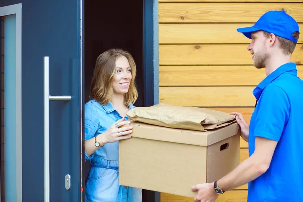 Homem de entrega sorridente em uniforme azul entregando caixa de encomendas ao destinatário conceito de serviço de correio. Sorrindo homem de entrega em uniforme azul — Fotografia de Stock