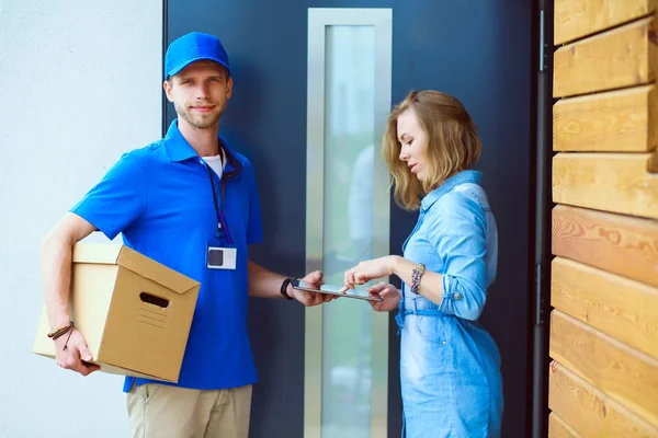 Mavi üniformalı gülümseyen kurye servis konseptine paket kutusu teslim eden teslimatçı. Mavi üniformalı gülümseyen teslimatçı.