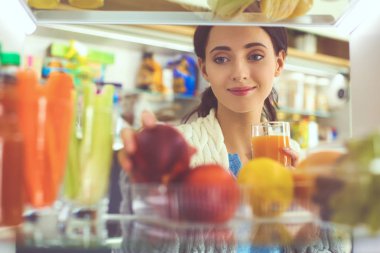 Sağlıklı yiyecek, sebze ve meyvelerle dolu açık buzdolabının yanında duran kadın portresi. Kadın portresi