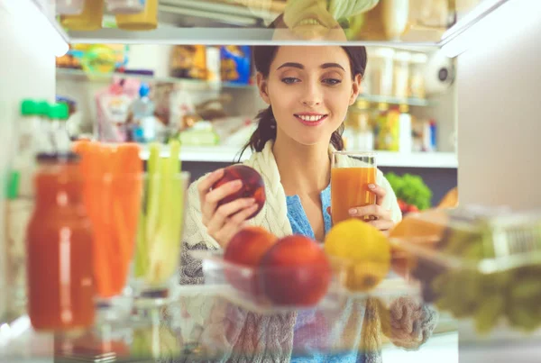Sağlıklı yiyecek, sebze ve meyvelerle dolu açık buzdolabının yanında duran kadın portresi. Kadın portresi
