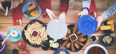 Ahşap masada otururken birlikte yemek yiyen bir grup insanın üst düzey görüntüsü. Masada yemek var. İnsanlar fast food yiyor..