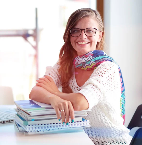 Kitapların arasında bir masada oturan genç bir kadın. Öğrenci