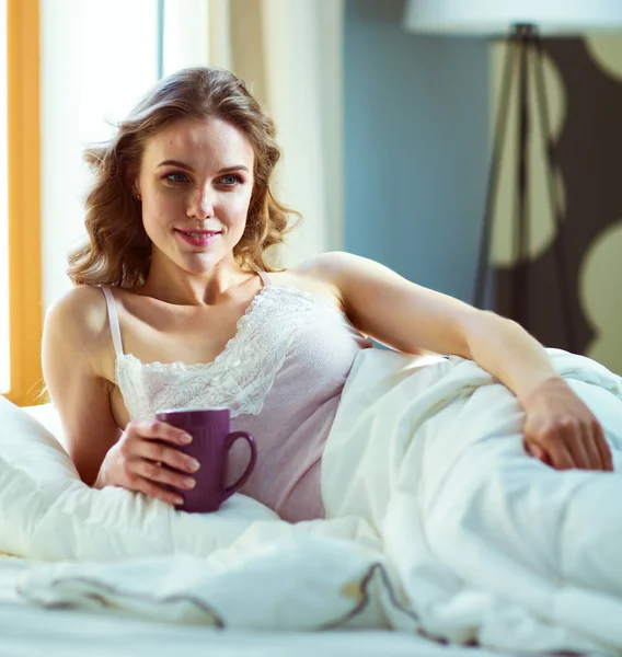 Young woman drinking cup of coffee or tea while lying in bed. — Stock Photo, Image