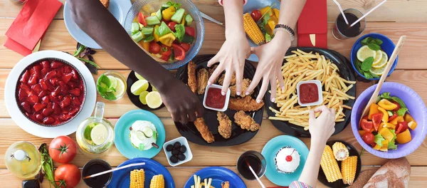 Ahşap masada otururken birlikte yemek yiyen bir grup insanın üst düzey görüntüsü. Masada yemek var. İnsanlar fast food yiyor..