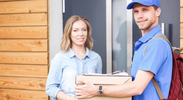 Repartidor sonriente con uniforme azul que entrega la caja de paquetes al destinatario: concepto de servicio de mensajería. Repartidor sonriente en uniforme azul —  Fotos de Stock