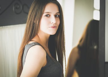 Genç kadın kendini evde aynada yansıma arıyor.