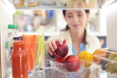 Sağlıklı yiyecek, sebze ve meyvelerle dolu açık buzdolabının yanında duran kadın portresi. Kadın portresi