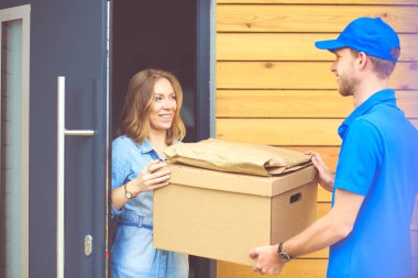 Mavi üniformalı gülümseyen kurye servis konseptine paket kutusu teslim eden teslimatçı. Mavi üniformalı gülümseyen teslimatçı.