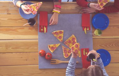 Ahşap masada otururken birlikte yemek yiyen bir grup insanın üst düzey görüntüsü. Masada yemek var. İnsanlar fast food yiyor..