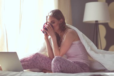 Dizüstü bilgisayar ile yatakta oturan genç güzel kadın