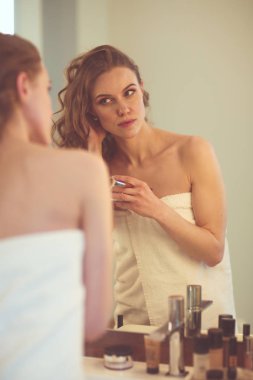 Genç bir kadın aynaya bakıyor ve makyaj yapıyor..