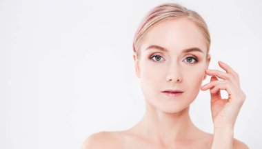 Mutlu gülümseyen genç bir kadının portresi tenine dokunuyor ya da krem sürüyor, beyaz arka planda izole edilmiş.