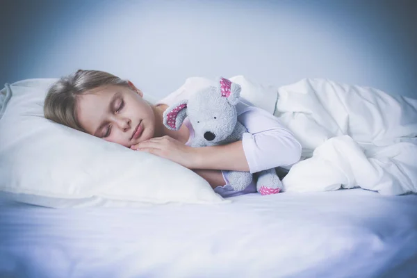 Child little girl sleeps in the bed with a toy teddy bear.