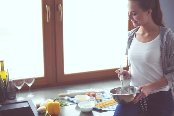 Eine junge Frau bereitet in der Küche Pfannkuchen zu, während sie am Tisch steht. Frau in der Küche. Kochen in der Küche. — Stockfoto