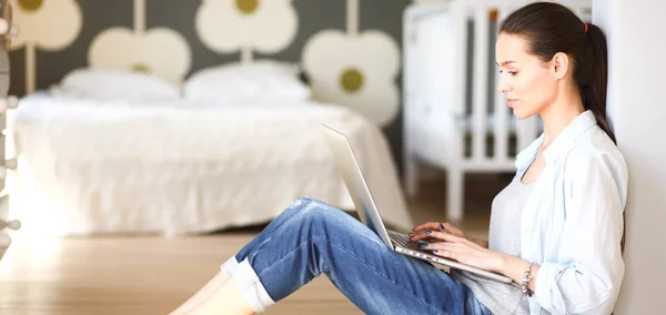Young woman sitting on the floor near childrens cot with laptop. Young mom — Stock Photo, Image