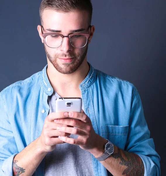 Smiling young man holding phone while text messaging — Stock Photo, Image