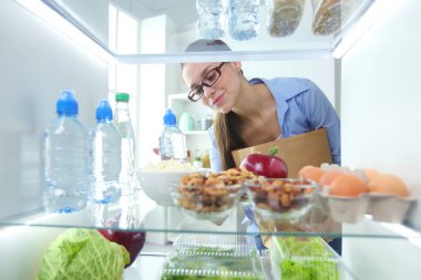 Sağlıklı yiyecek, sebze ve meyvelerle dolu açık buzdolabının yanında duran kadın portresi..