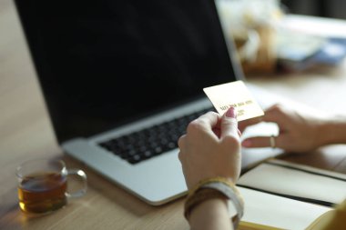 Kredi kartı tutan ve dizüstü bilgisayar kullanan genç bir kadın. Çevrimiçi alışveriş kavramı