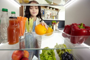 Sağlıklı yiyecek, sebze ve meyvelerle dolu açık buzdolabının yanında duran kadın portresi. Kadın portresi