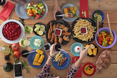 Ahşap masada otururken birlikte yemek yiyen bir grup insanın üst düzey görüntüsü. Masada yemek var. İnsanlar fast food yiyor..